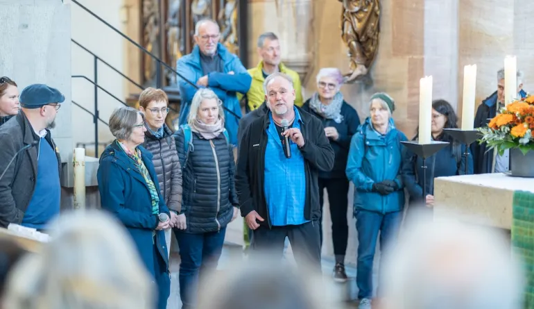 Michael Kaminski bedankt sich bei allen Besucher:innen, er steht in einer Gruppe mit einem Mikrofon in der Hand und spricht
