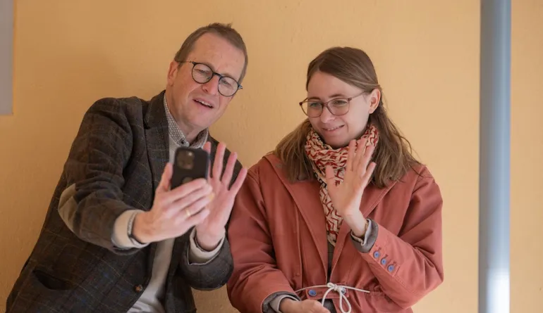 zwei teilnehmende winken ins Handy und nehmen einen Film auf