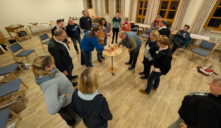 Ein Tisch in der Mitte, auf dem Holzfiguren stehen auf den die teilnehmenden gemeinsam schauen