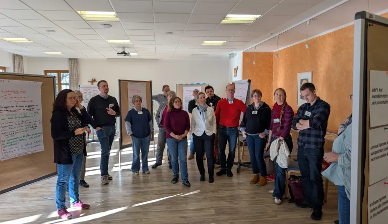 die teilnehmenden stehen im Halbkreis und blicken gemeinsam auf eine Stellwand