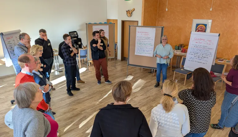 eine Person steht an Moderationswänden in der Mitte, die anderen Personen im Halbkreis drum herum