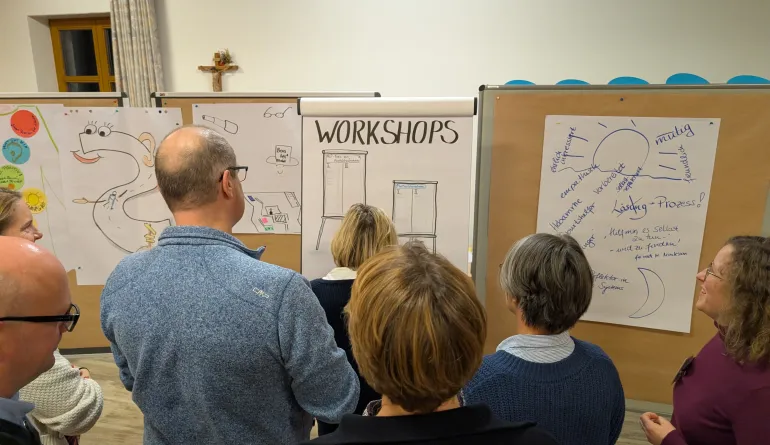 Menschen lesen an Stellwänden Arbeitsergebnissen, der Betrachter blickt mit ihnen auf die Ergebnisse