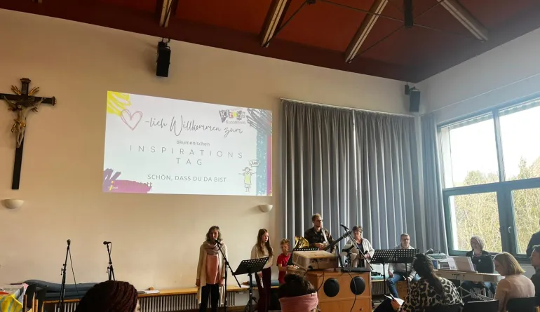 Gemeindesaal mit einer großen Folienbild: Herzliche Willkommen